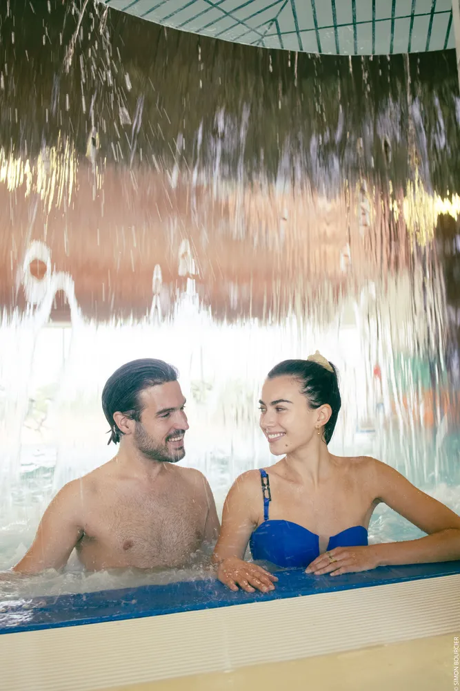 Couple complice sous une cascade d'eau relaxante dans le parcours marin d'une thalasso en Vendée.
