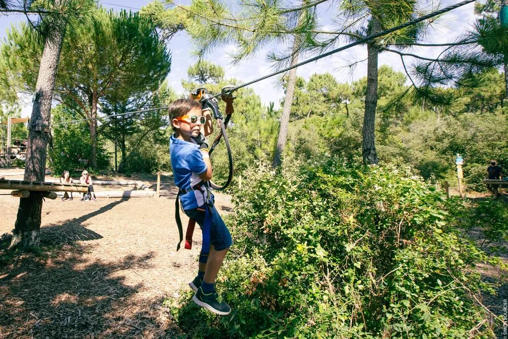 Jeune garçon avec lunettes de soleil sur une tyrolienne en forêt, parcours accrobranche enfant