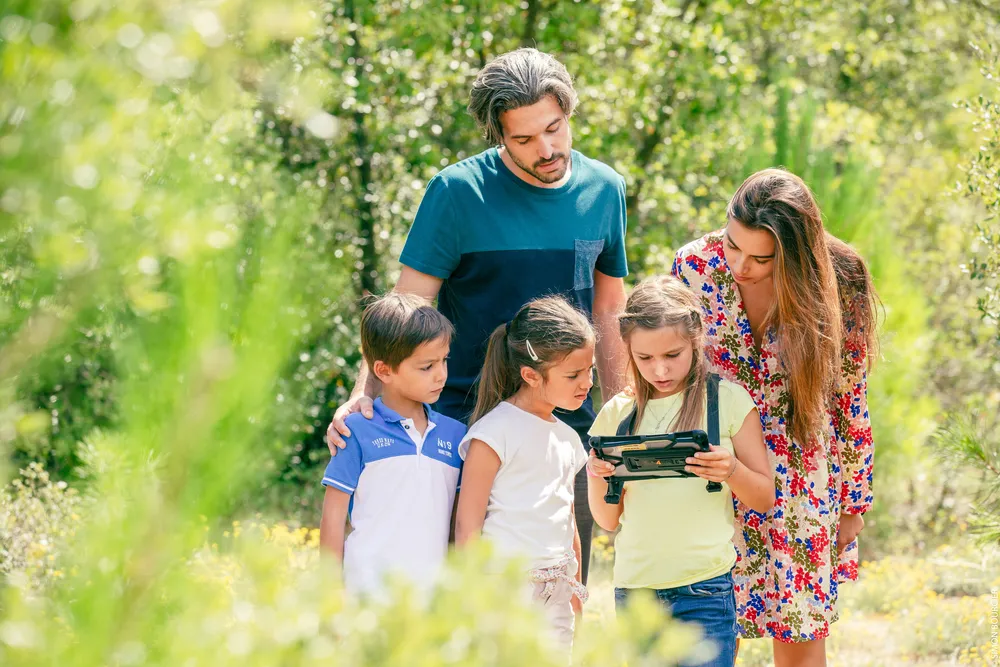 Famille avec trois enfants regardant une tablette lors d'un jeu de piste en forêt